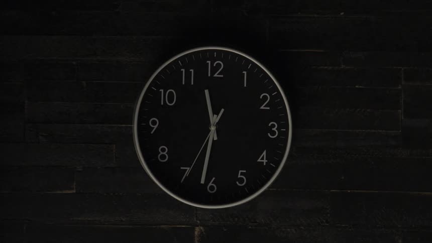 An analog wall clock hanging on a wall showing the time 1135 as the room suddenly shifts between brightness and darkness