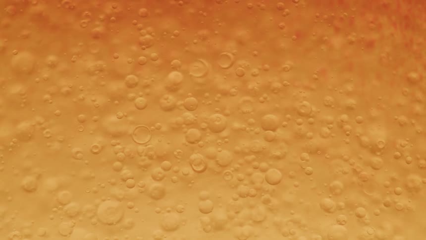 Golden liquid bubbles rise and swirl in an extreme closeup creating an abstract texture
