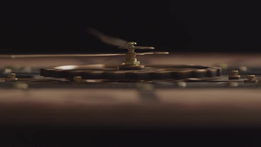 A closeup view shows the intricate brass gears and levers of a clock mechanism against a dark blurred background