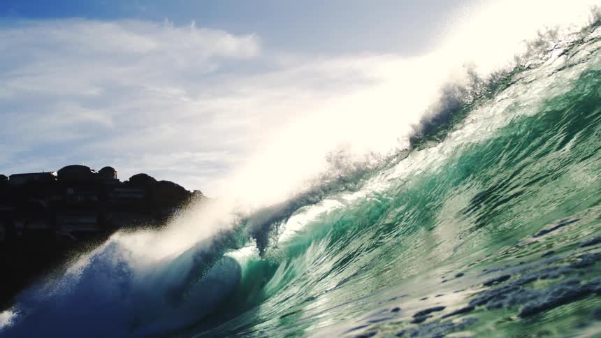 A big wave of crystalclear water and a blue sky with white clouds
