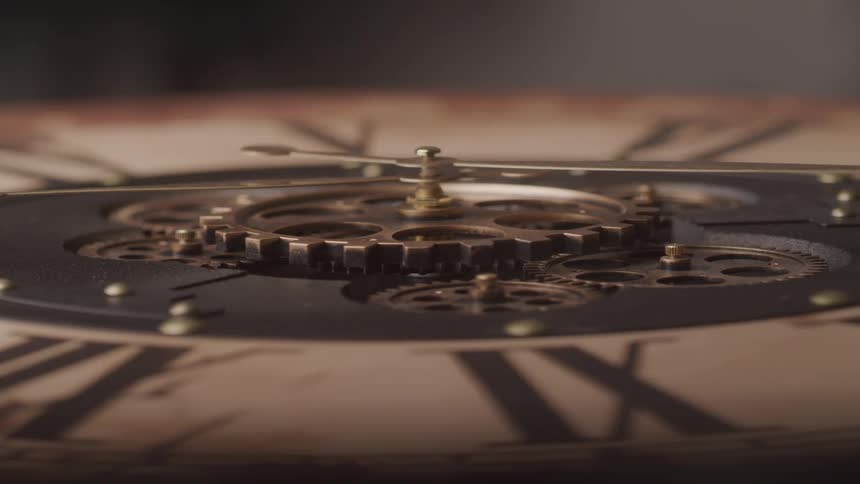 A closeup shot focuses on the intricate brass gears of an antique clock revealing the detailed mechanics and ornate hands against a roman numeral dial
