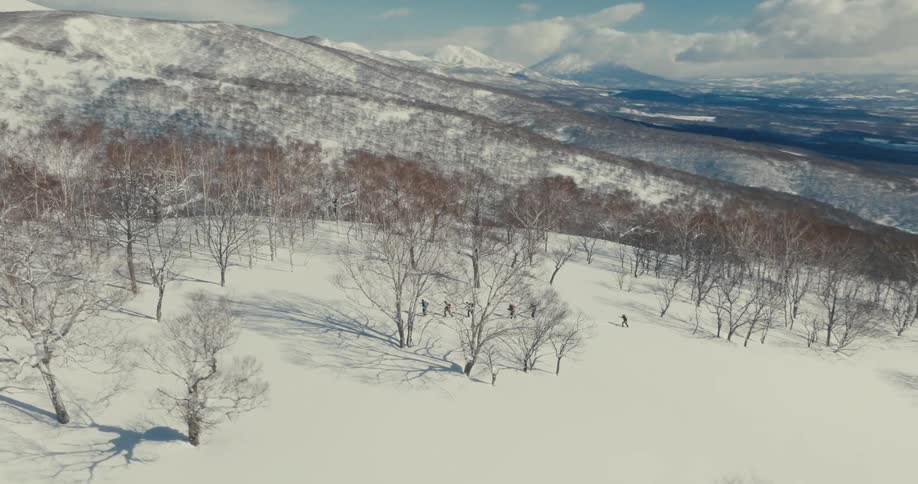 Aerial of a group of people hiking up a snow covered slope on a mountain