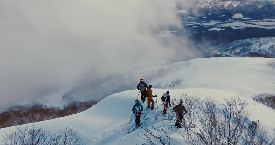 A group of skiers stand atop a snowy mountain ridge preparing to descend
