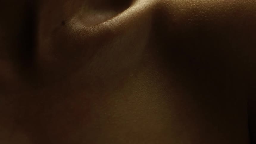 A bare shoulder visible in a closeup shot with light highlighting the skins texture against a dark background