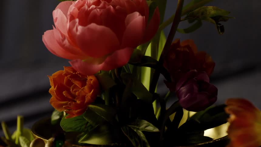 A moody dark closeup of a floral arrangement in a bowl featuring pink and orange flowers mushrooms and a small beetle