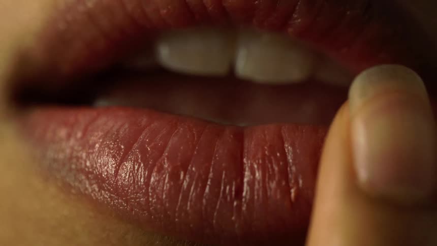 Extreme close up of a womans lips as she pats her lips with her fingers