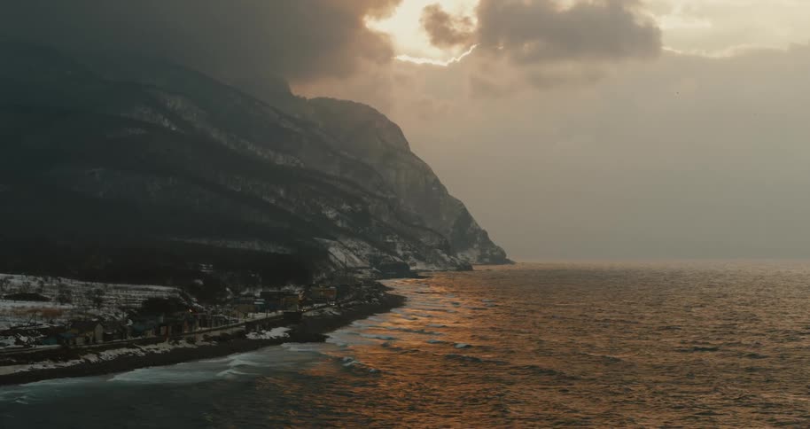 Dramatic coastal cliffs meet snowy shores under a golden cloudy sunset