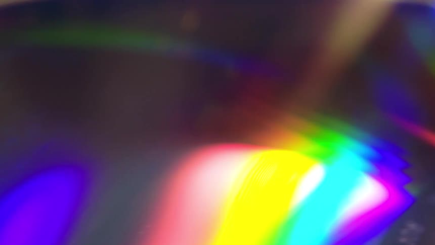 A closeup video captures a cd being slowly moved from its center toward the outer edges revealing shifting rainbow reflections across its shiny surface