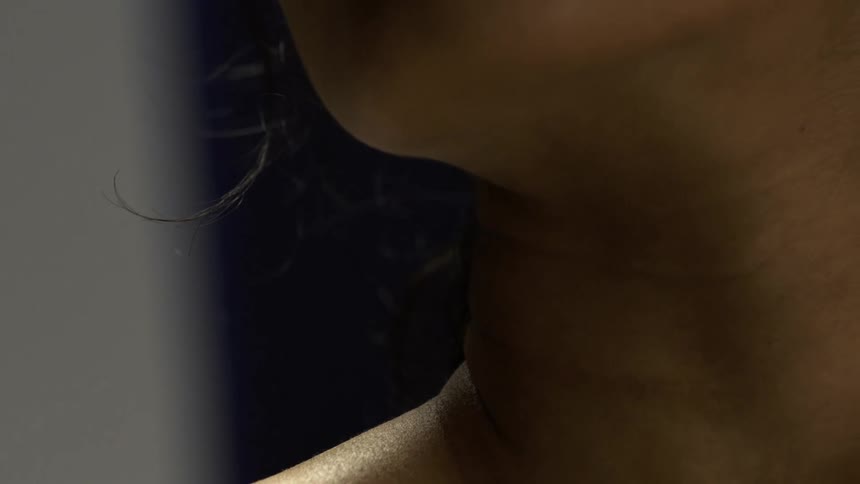 Close up of a womans chest and neck area as she stands in a dark room