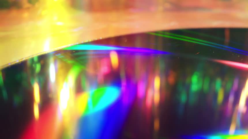 A circular cd or dvd reflects a vibrant spectrum of rainbow colors and bright light sources across its dark glossy surface