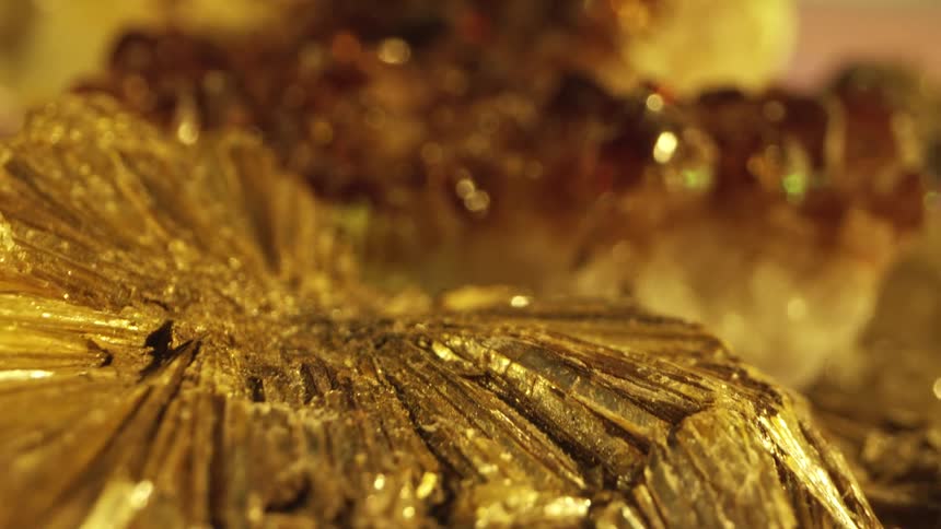 A closeup shot focuses on a cluster of dark shimmering crystalline formations with hues of amber and brown illuminated by a warm golden light