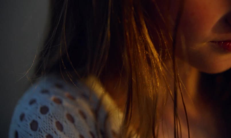 Close up partial view of a young girl's face as her hair blows in the breeze and the setting sun gives her skin a copper glow.
