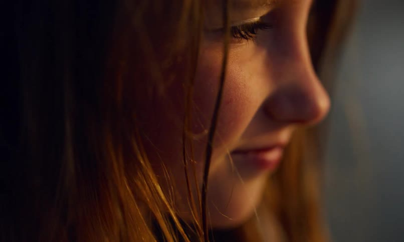 Close up of the face of a young girl as she squints into the fading light of the sunset and then looks down thoughtfully.