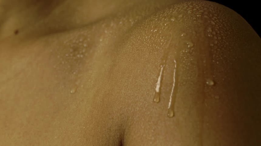 Close up of a womans shoulder sprayed with water and the water droplets flowing down her arm