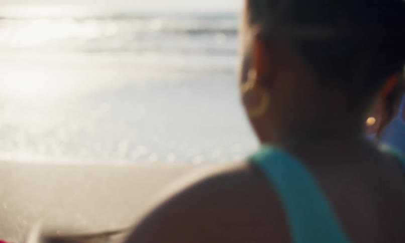 Close up of a young black girl dropping sand from her hands as she plays on the beach next to another young girl who is building a sand pile.