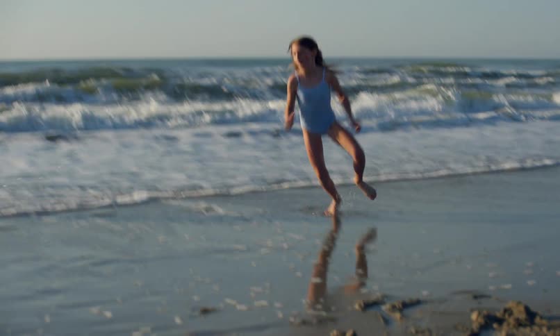 A group of children playing and running in the sand and surf at the seaside as the sun is going down on a clear summer day.