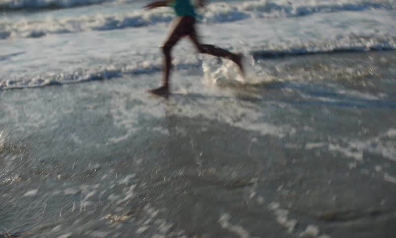 A group of diverse little kids running and splashing in the loamy surf along the seashore at sunset.