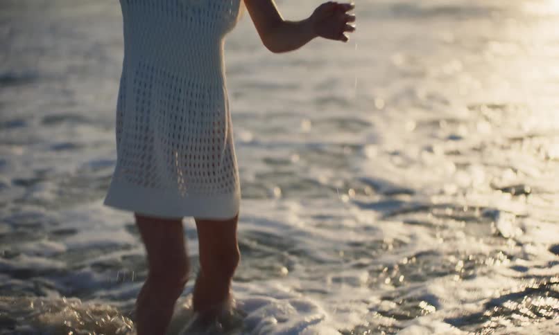 Slow-motion clip of two diverse little girls standing at the shoreline of a beach at sunset and happily kicking and splashing against the waves as they come in.