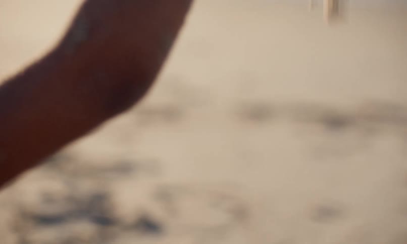 Close up of a little black girl sitting on the beach on a sunny day and exploring the texture and feel of sand on her skin as she drops it from her hands to her legs.