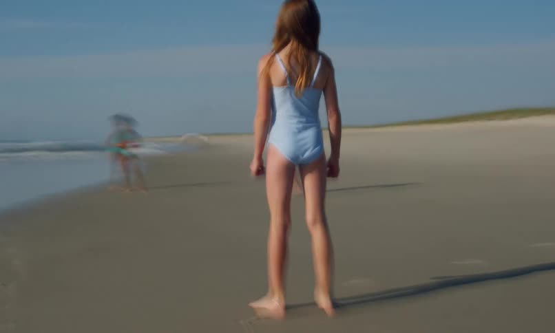 A shaky fast-forward motion blur clip of three children running around and playing together in the sand and surf at a beach on a sunny day.