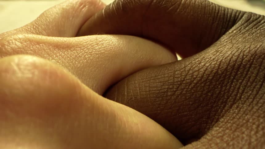 Close up of the fingers of a black and white person interlocked and placed on a surface