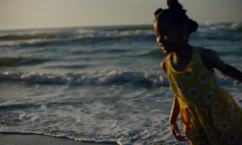 Slow motion of two young girls happily playing chase in the sand and surf on a beach at sunset.