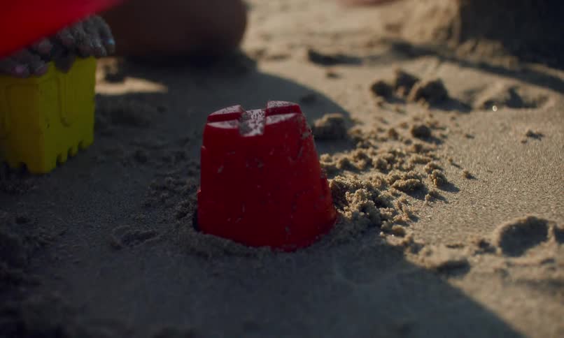 Close up of children's hands at the beach filling colorful plastic molds with wet sand to create sandcastles.