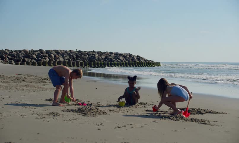 A group of children play and dig in the sand with plastic shovels and pails at a quiet beach on a sunny summer day.