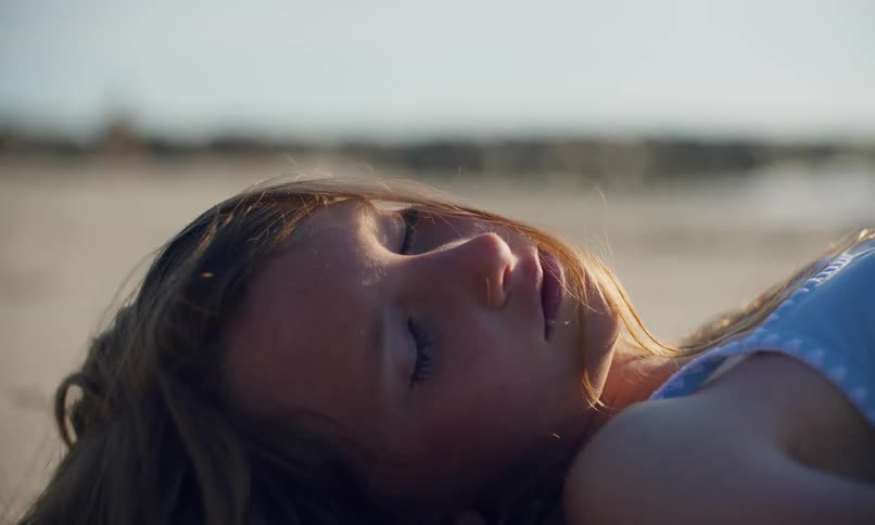 A young girl is laying in the sand on a quiet beach with the sun on her face and long hair gently blowing in the breeze.