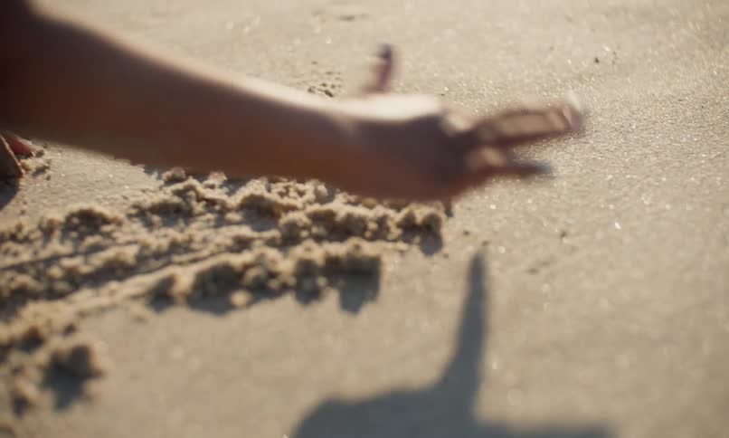 A little black girl writes her name in the sand with her finger as she plays on the beach at sunset.