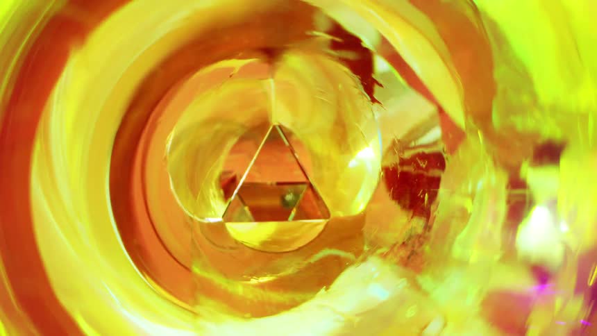 A closeup view looking down a triangular prism with vibrant swirling yellow and orange reflections