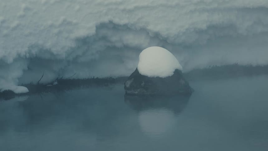 A snowcovered rock sits quietly beside a still misty riverbank in a frozen landscape