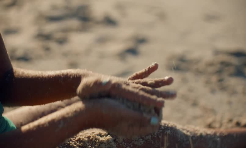 A young girl sitting in the sand at the beach and playing with the textures and sensory feeling of the sand on a sunny day.