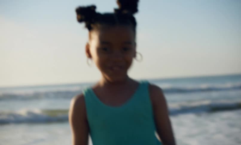 A little black girl in a blue swimsuit sprints excitedly in the surf to playfully escape the waves coming in on the beach at sunset.