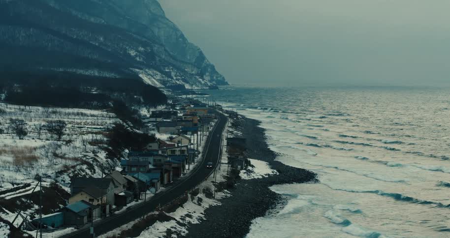 A scene at a snowy black sand beach with the waves breaking on the shoreline and snow on the land
