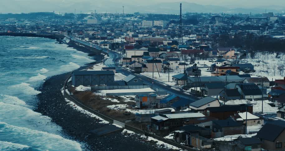 A snowcovered coastal town stretches along a curving shoreline under a cold overcast sky