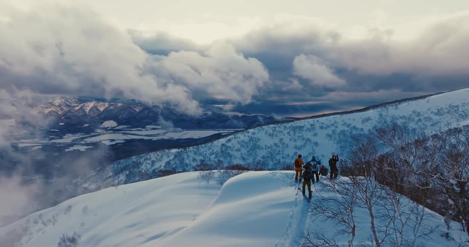 Group of people standing on a snowy mountain ridge under dramatic clouds
