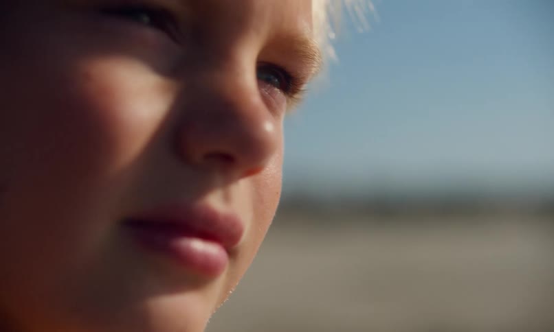 Close up of a young blonde boy at the beach on a summer day with sand in his hair and sun on his face.