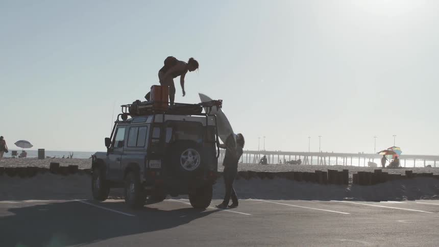Surfboard is unloaded from vehicle roof