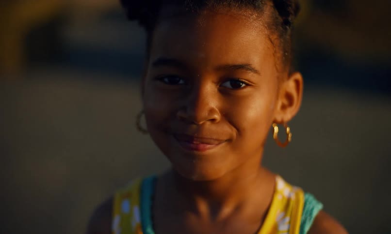 Portrait of a young girl of color wearing hoop earrings and bright summer colors and giving a playful smile while standing outdoors at sunset.