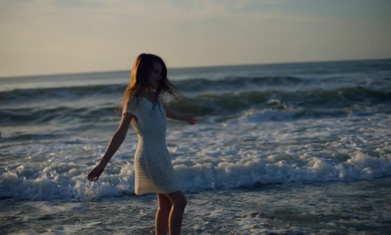Slow motion of two young, happy girls twirling on the beach as ocean waves crash onto the shore at sunset.
