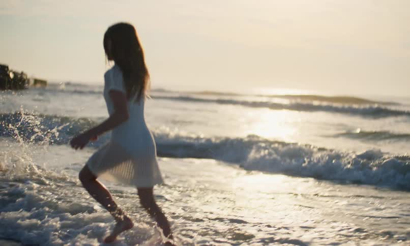 Slow motion of two diverse young girls joyfully running and splashing in the surf as the ocean waves roll in at sunset on the beach.