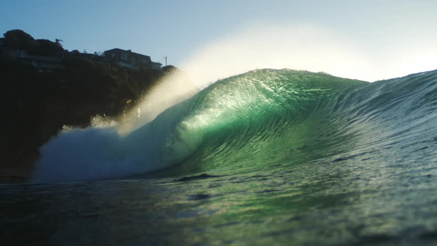 Surfer lies on their board while a large wave swells and breaks beneath them