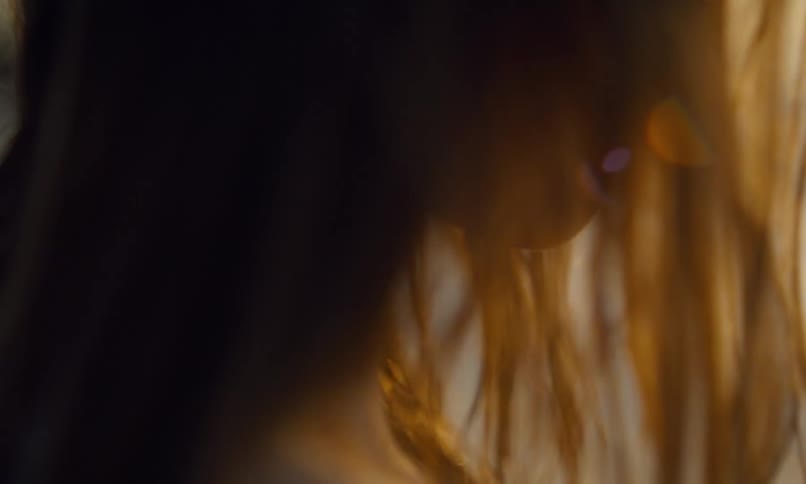 A young girl in profile stands on a beach at sunset looking at a piece of translucent turquoise seaglass as the evening sun rays shine through her damp hair.