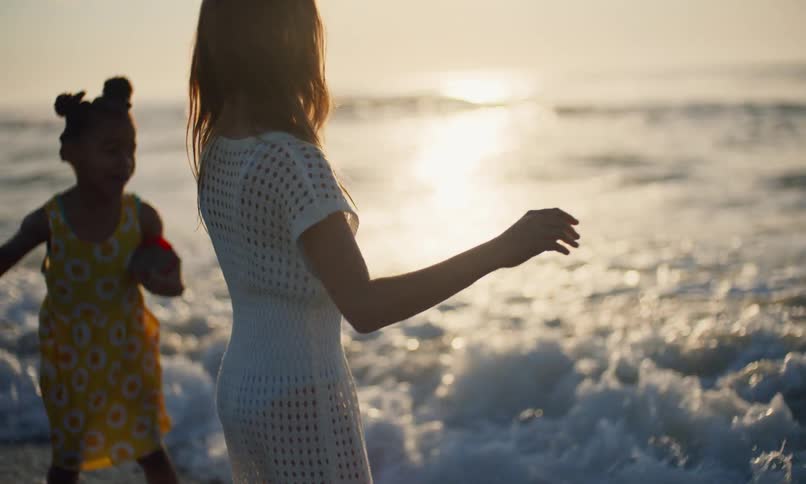 Two young girls kick the waves and jump in the surf as they happily play in the water on the beach at sunset.