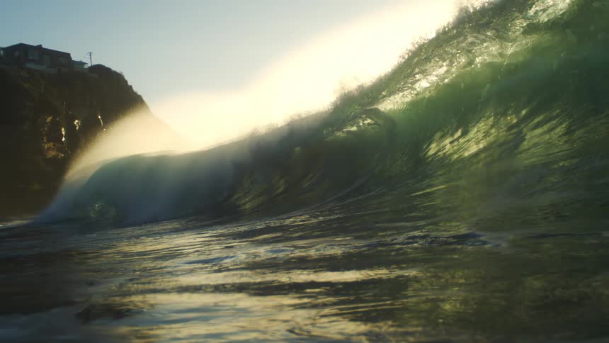 A large wave moves by the cliff on a sunny day