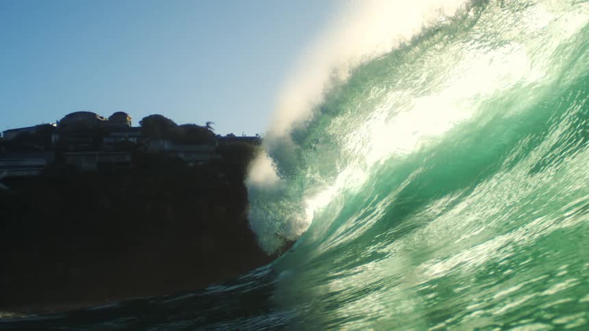 Crystal clear turquoise blue wave breaking in the ocean and the coast in the background