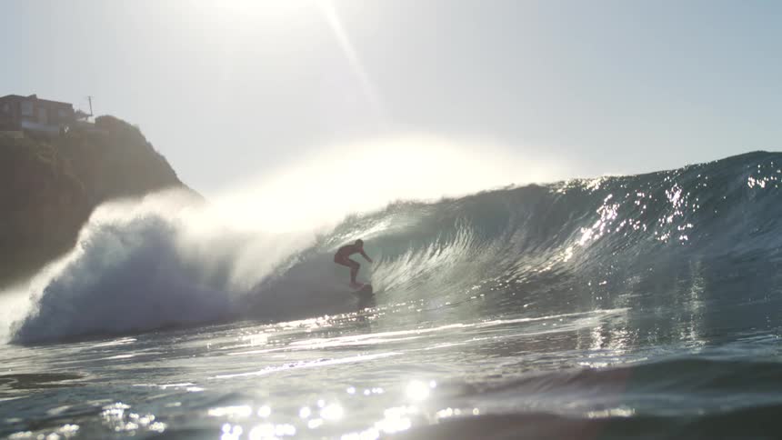 A person riding a massive wave forming in the ocean under the bright midday sun