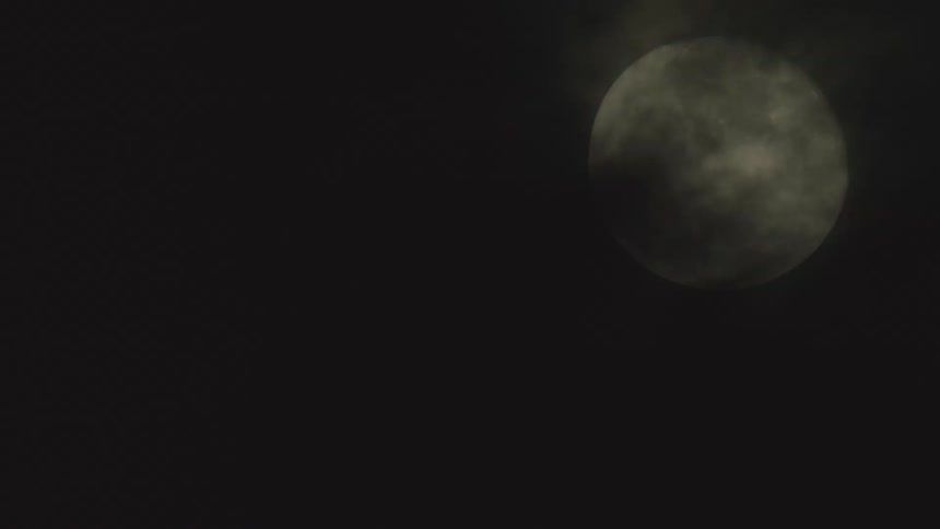 A large full moon is partially obscured by dark clouds against a black night sky