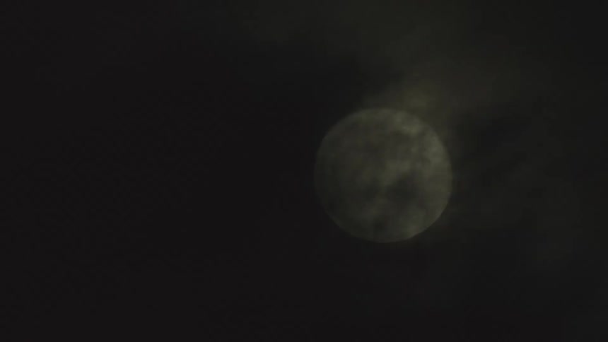 A large full moon is partially obscured by dark clouds against a black night sky